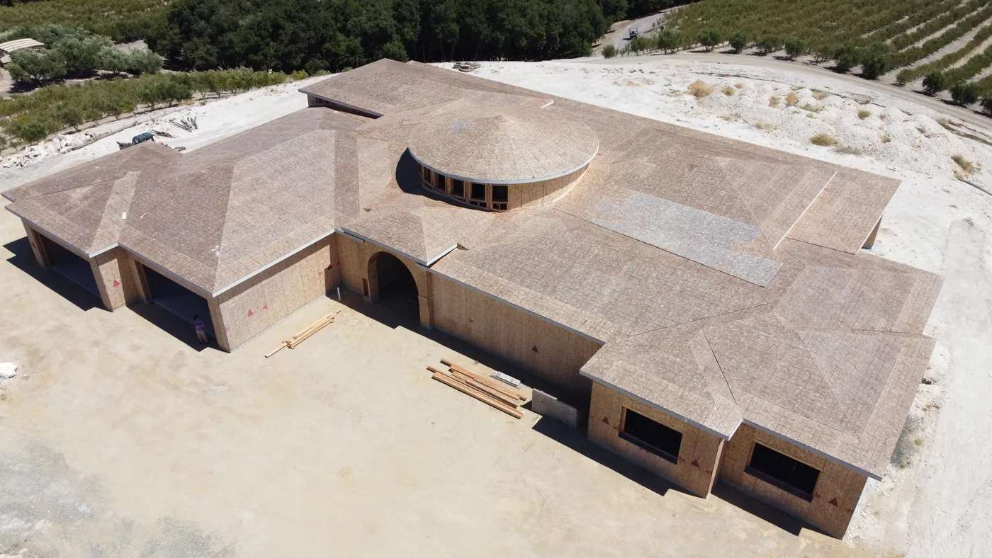 Drone photo of a large house under construction, framed and sheathed, with a round tower at its centre